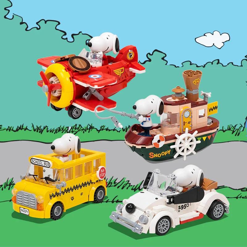 A group of four Peanuts-themed toy vehicles, including a red airplane, a yellow school bus, a brown boat, and a white car, are depicted in the image.