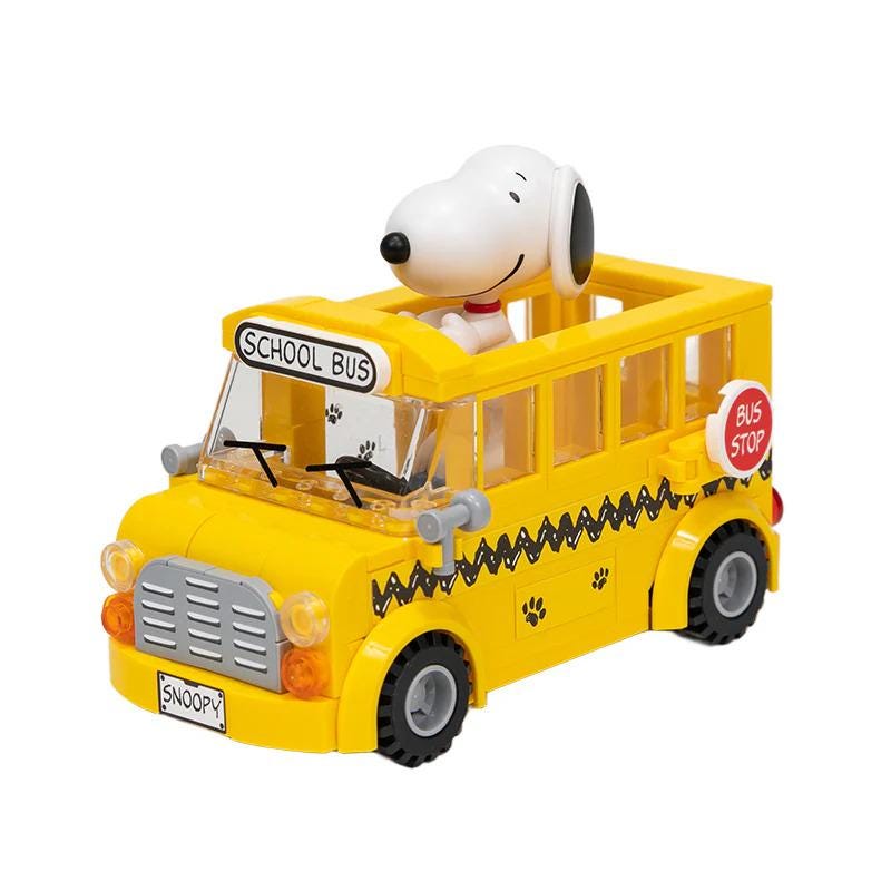 A yellow toy school bus with a Snoopy dog figurine sitting in the driver's seat.
