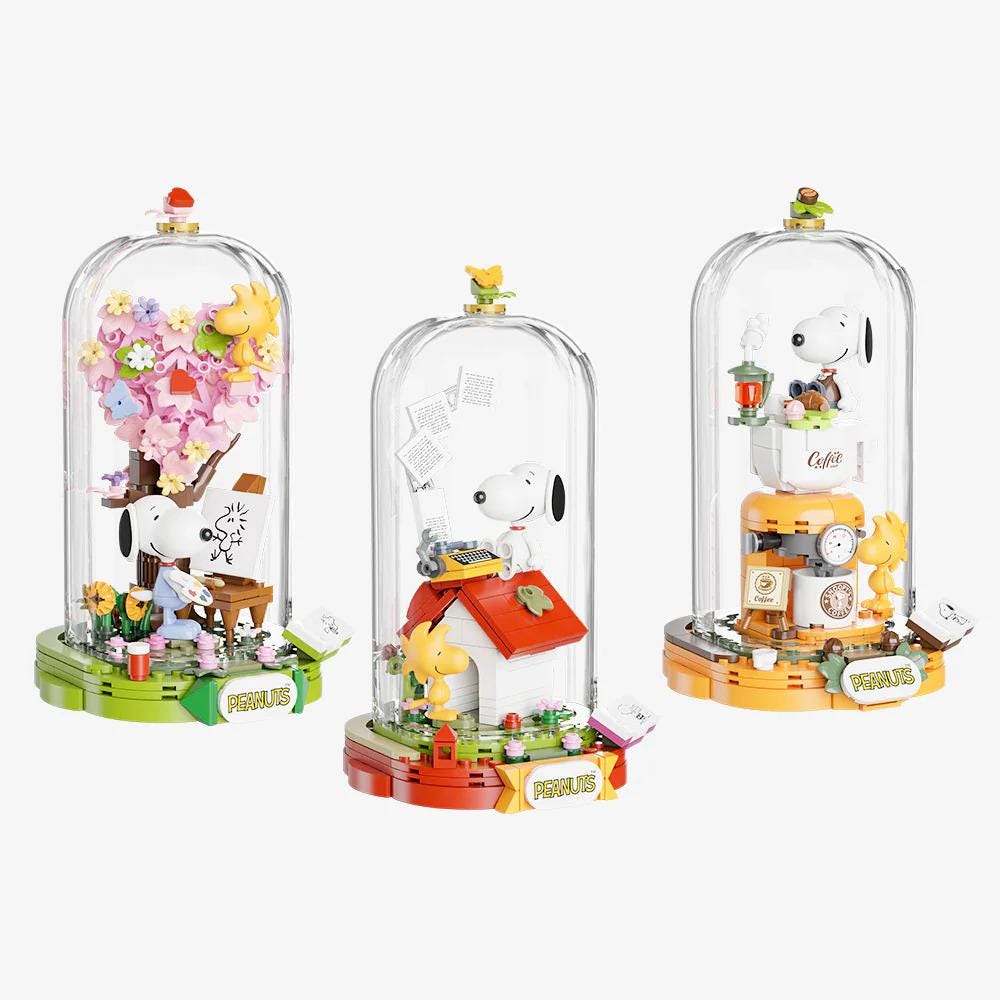 Three glass cases containing Peanuts characters and various objects, such as a tree, a house, and a clock.