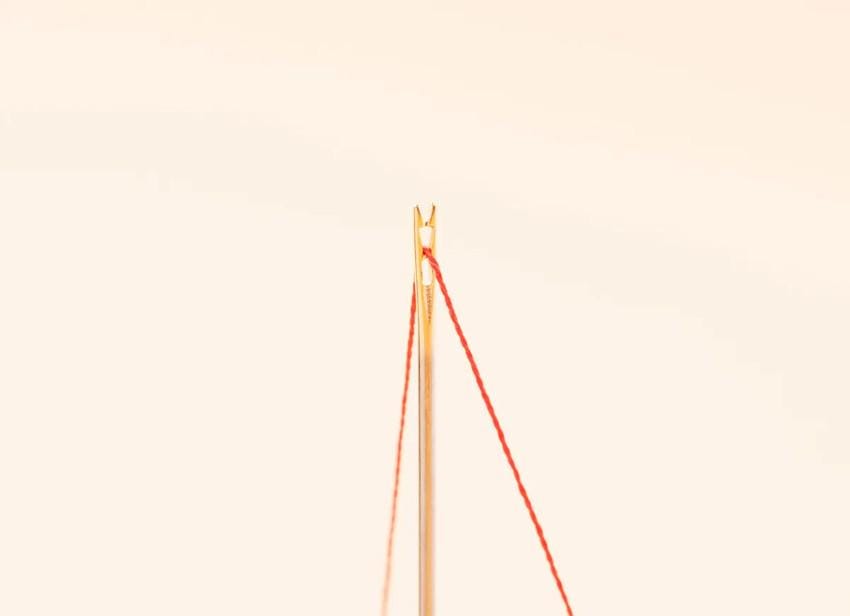 A close-up view of a needle with red thread, against a light background.