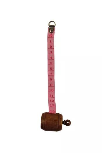 A pink measuring tape with numbers on it, attached to a wooden barrel.