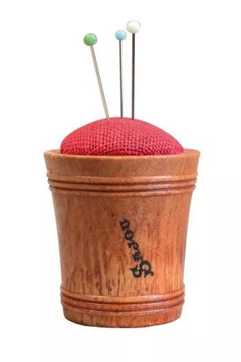 A wooden sewing cup with a red cushion and three needles sticking out of it.