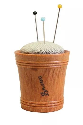 A wooden cup with a white cloth inside, containing three needles.