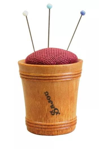 A wooden cup with a red cushion and three needles sticking out of it.