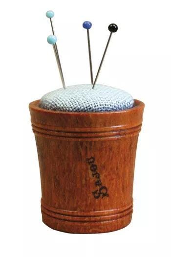 A wooden cup with a white cloth inside, containing several needles.