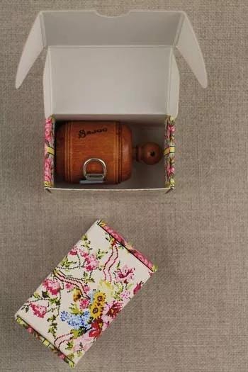 a wooden object, possibly a small wooden barrel or container, placed inside a white box with a floral pattern.