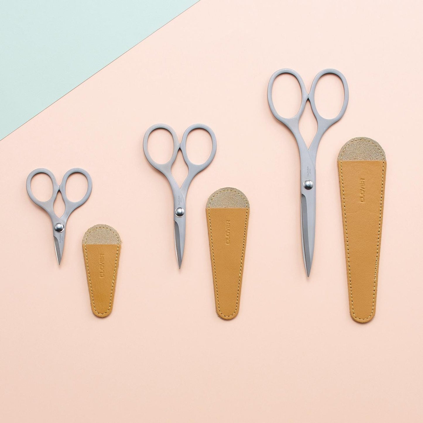 a collection of scissors and leather pouches arranged on a light pink background.