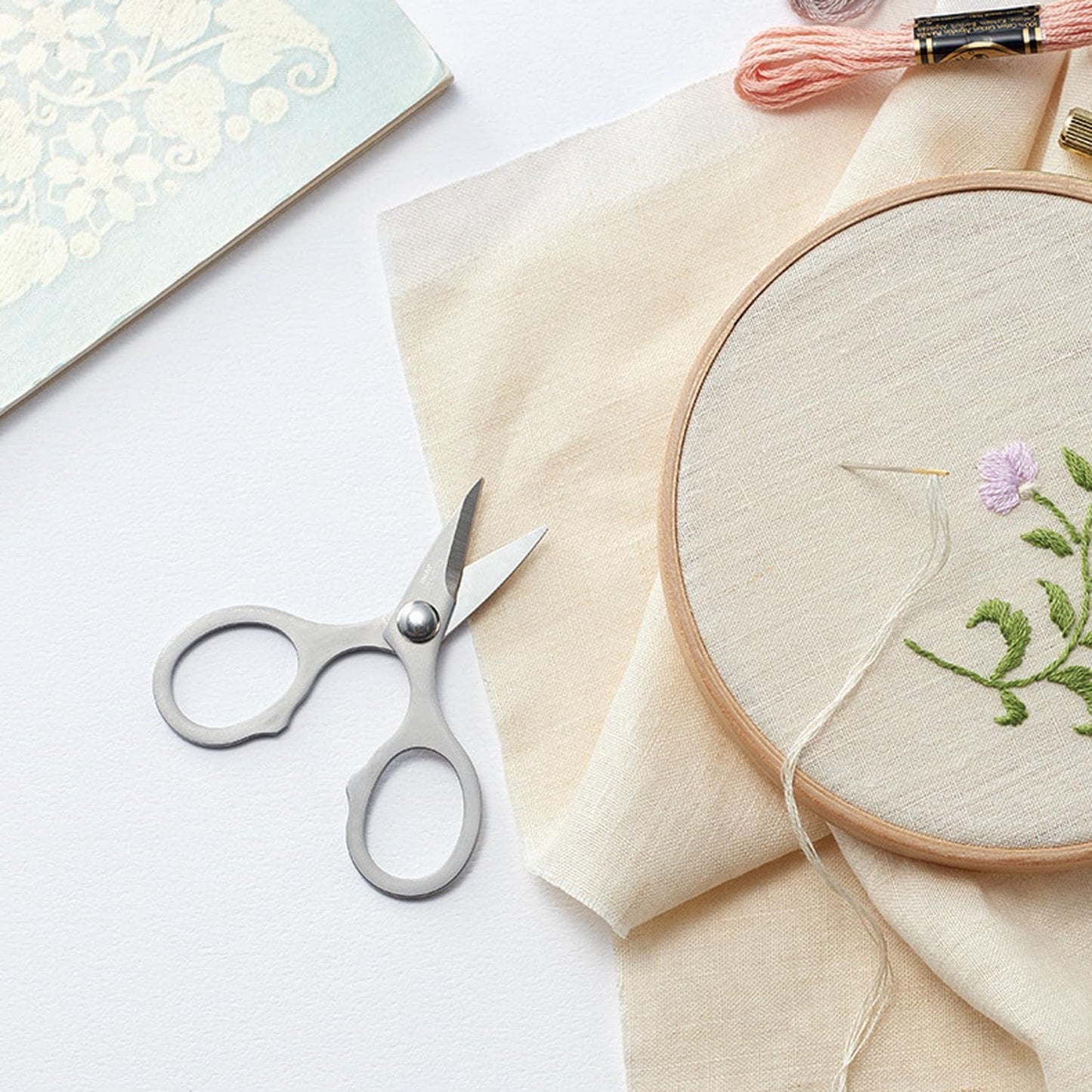 a pair of scissors, a piece of embroidery, and some thread on a white background.