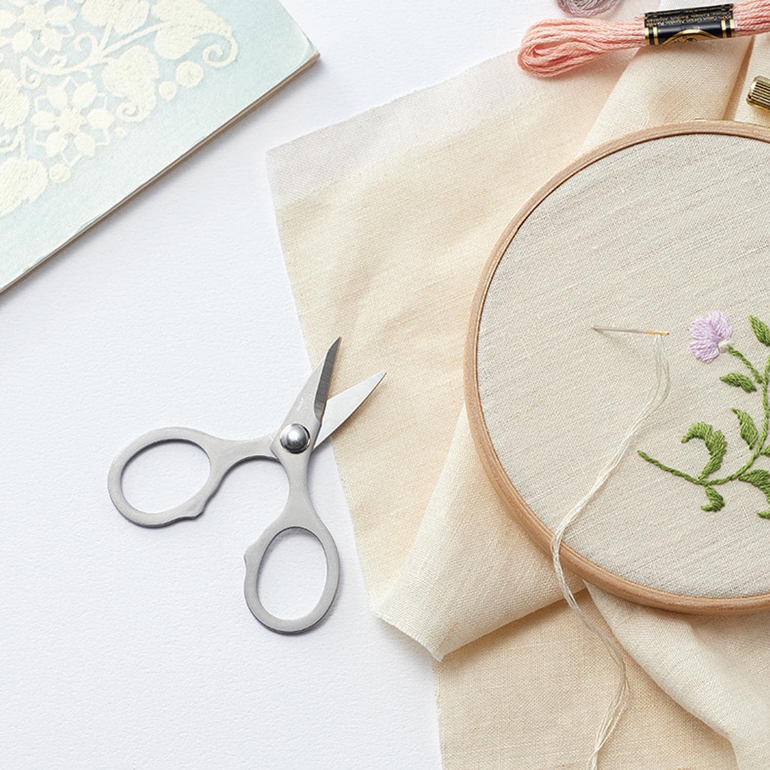 a pair of scissors, a piece of embroidery, and some thread on a white background.