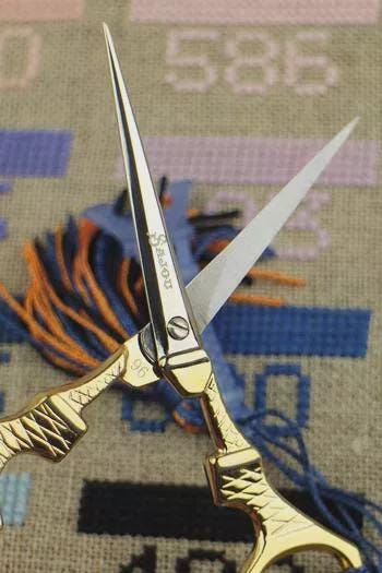 A pair of gold-colored scissors with a silver blade is prominently displayed against a background of colorful embroidery.