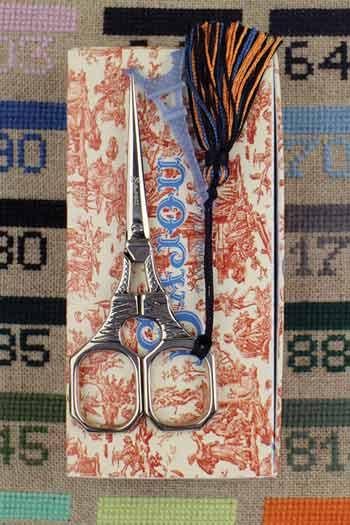 A pair of silver scissors with a black tassel is placed on top of a patterned box, which appears to be a sewing kit or craft box.