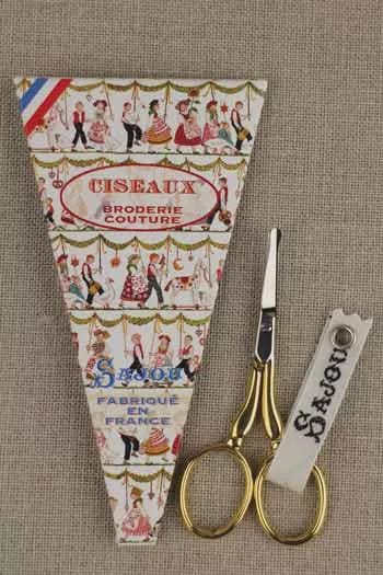 a pair of gold scissors and a small decorative box with a picture of people on it.