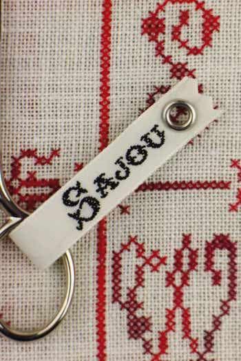 a close-up view of a white tag with the name "Sajou" printed on it, attached to a pair of silver scissors.