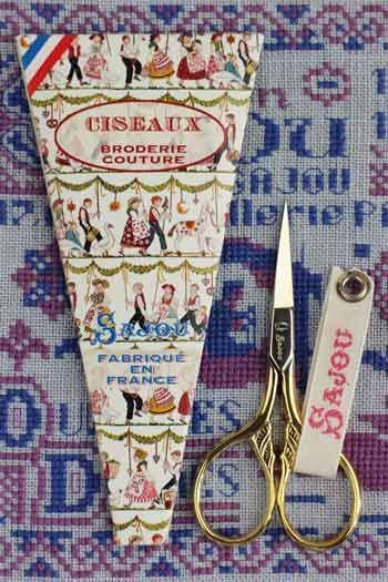 a pair of gold scissors and a decorative paper with a pattern of people and various objects, all placed on a patterned background.