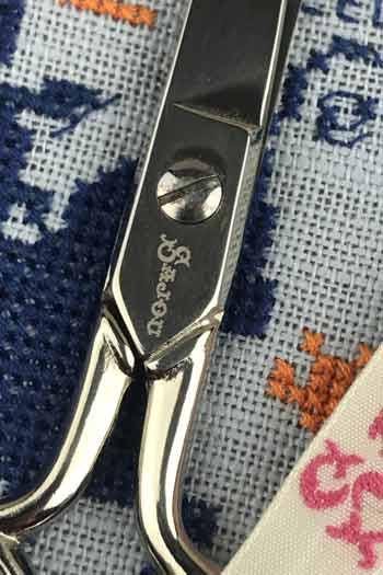 A close-up view of a pair of scissors with a metal handle and blades, resting on a fabric surface with a patterned design.
