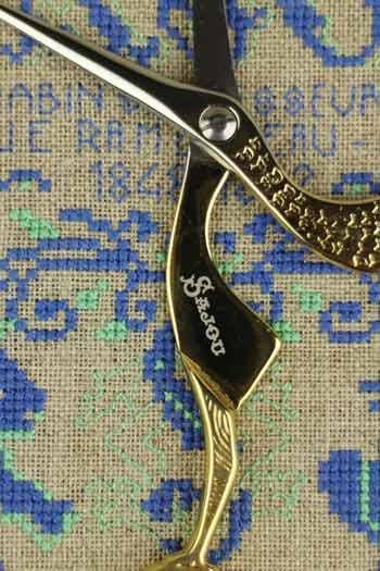 A close-up view of a pair of scissors with a decorative handle, resting on a textured fabric with a blue and green pattern.