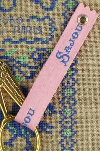 A pink keychain with the word "Saujour" printed on it, attached to a gold keyring.