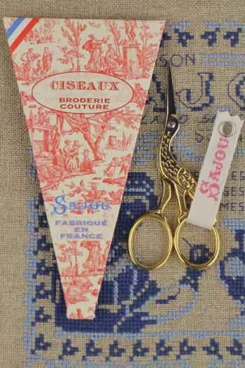 a pair of gold scissors and a red and white patterned box with the text "CISEAUX BRODERIE COUTURE" printed on it.