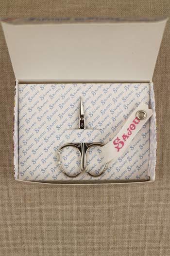 a pair of scissors and a box with a patterned paper inside, placed on a beige surface.