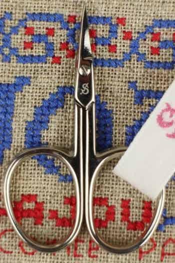 A pair of silver scissors with a blue and red embroidered pattern on a beige background.