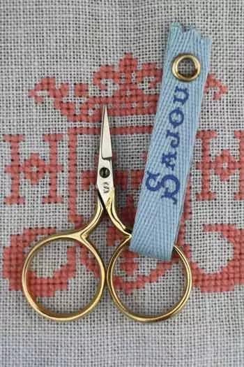 A pair of gold-colored scissors with a blue tag attached to them, resting on a red and white fabric background.