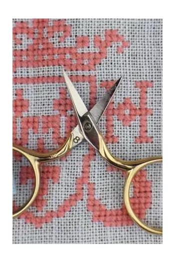A pair of gold-colored scissors with crossed blades rests on a red and white patterned fabric.