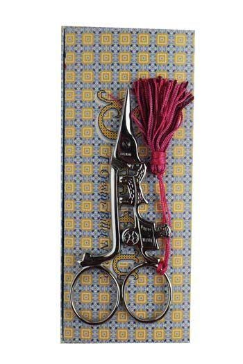 A pair of silver scissors with a tassel attached, displayed on a patterned background.