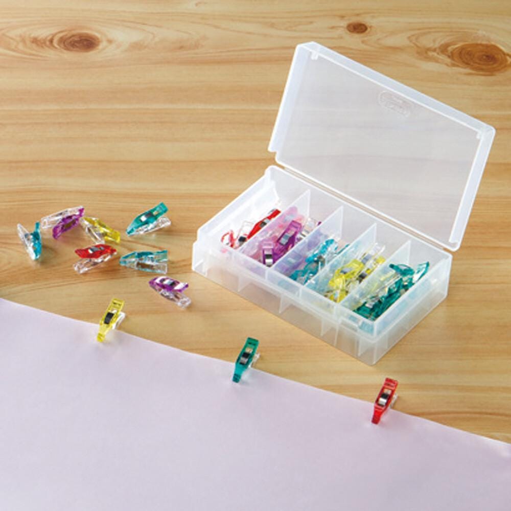 a clear plastic container filled with colorful plastic clips, with some of the clips scattered on a wooden surface.