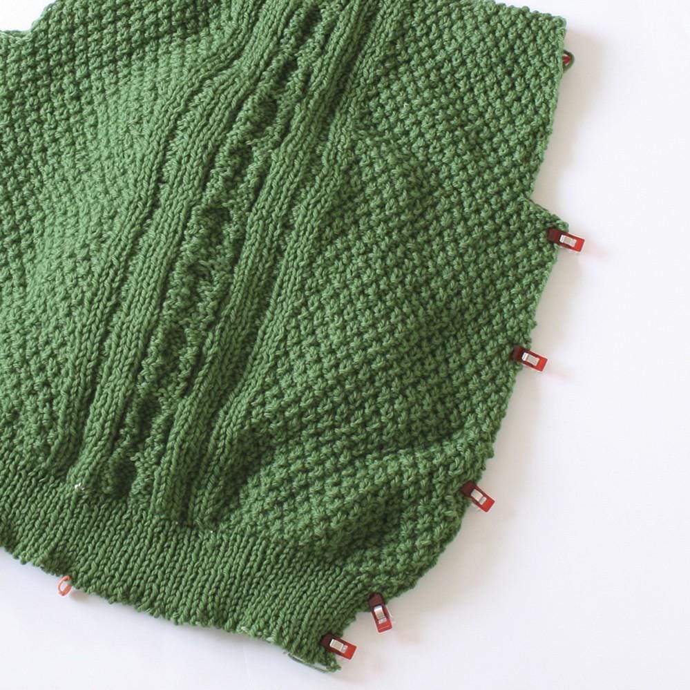 a close-up view of a green knitted fabric with red clips attached to it, suggesting it is being sewn or fastened together.