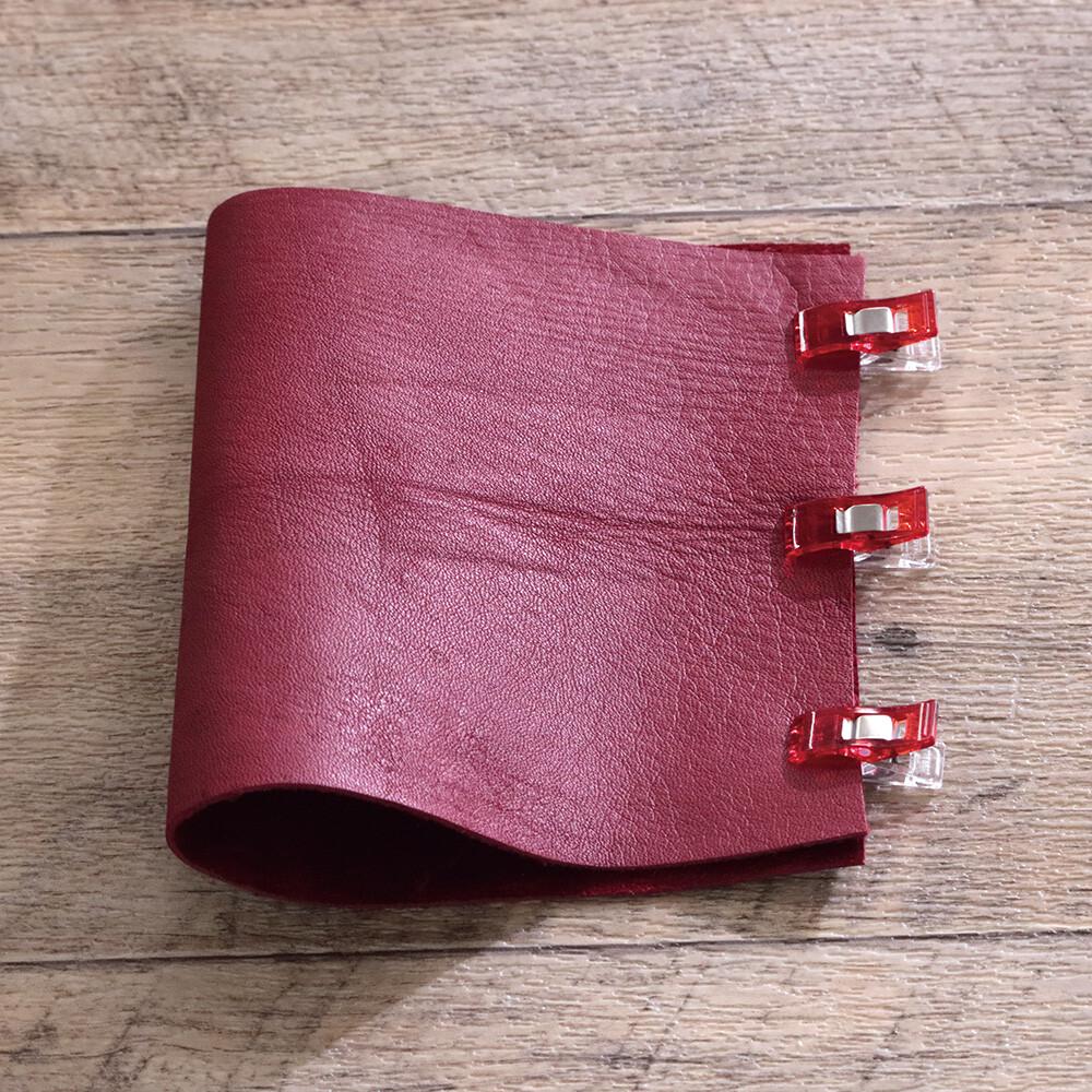A red leather-like material with red plastic clips attached to it, resting on a wooden surface.