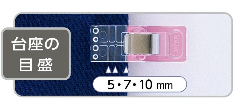 a clear plastic object with a pink component, placed on a blue fabric. The object appears to be a sewing or crafting tool, possibly a pin or a clip. The image contains text in Japanese, which translates to "The object is a clear plastic piece with a pink component, and it measures 5.7 mm in length."