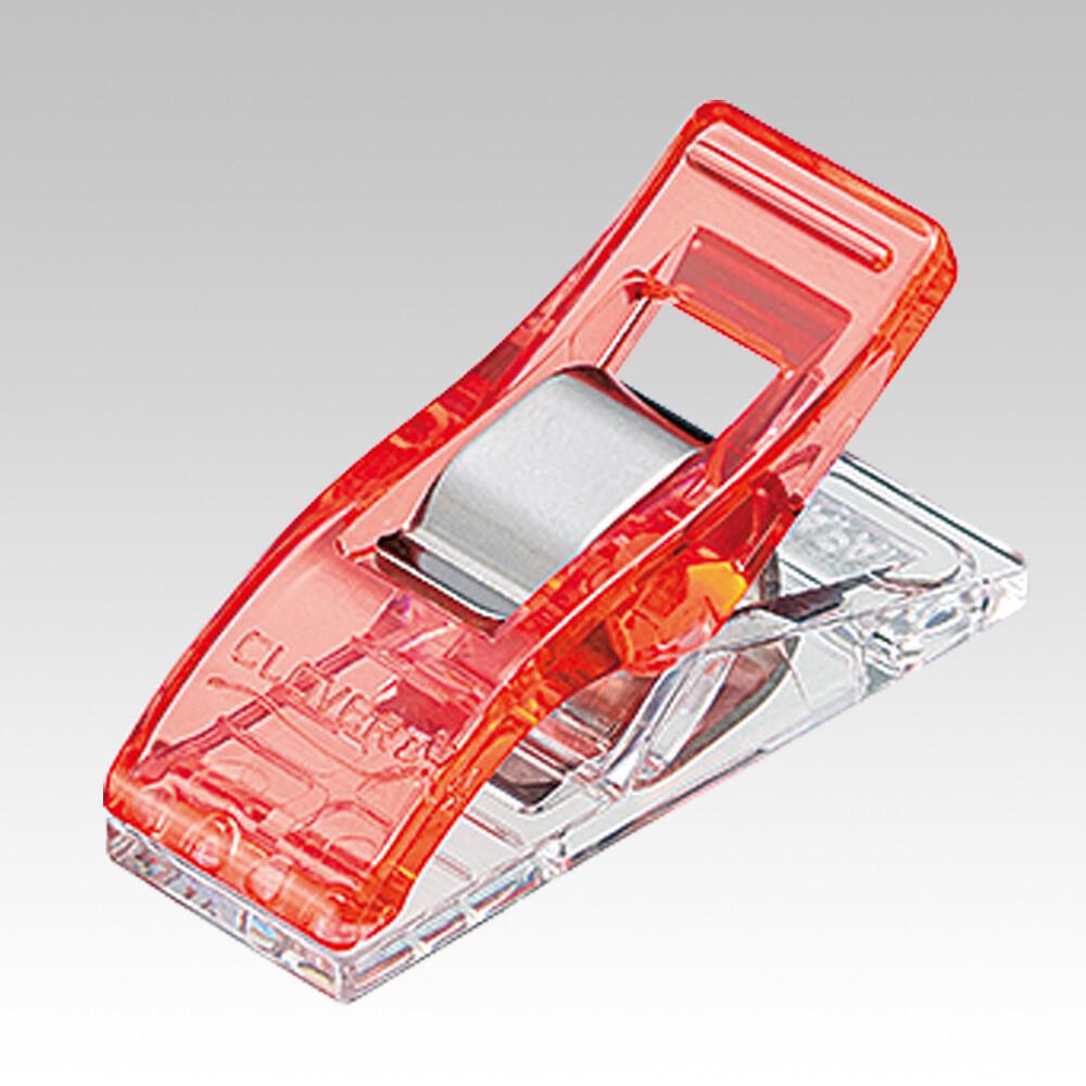 A red plastic clip with a silver metal piece attached to it, sitting on a clear plastic stand.