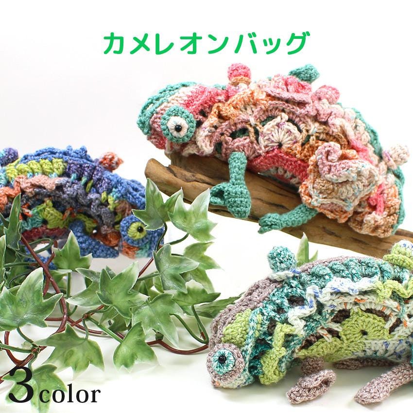 three crocheted chameleons in different colors - blue, pink, and green. The chameleons are displayed on a wooden surface, surrounded by green leaves.