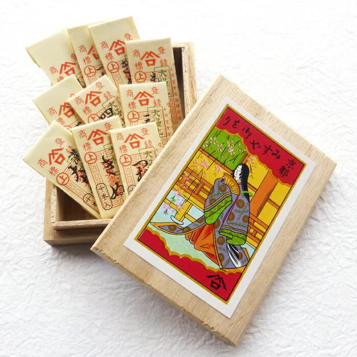 a wooden box with a colorful illustration of a woman in traditional Japanese attire, along with a set of small white cards with red and black designs inside the box.