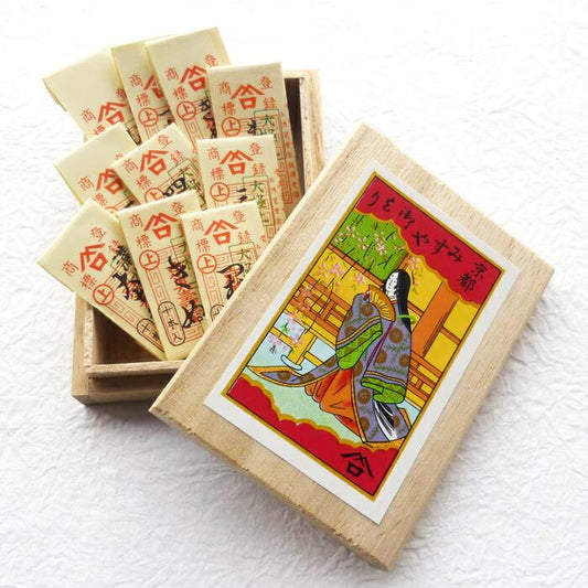 a wooden box with a colorful illustration of a woman in traditional Japanese attire, along with a set of small white cards with red and black designs inside the box.