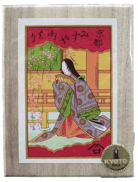The image is a framed illustration of a woman in traditional Japanese attire, sitting in a contemplative pose with a fan in her hand. The background features a colorful floral pattern, and there is Japanese text at the top of the frame.