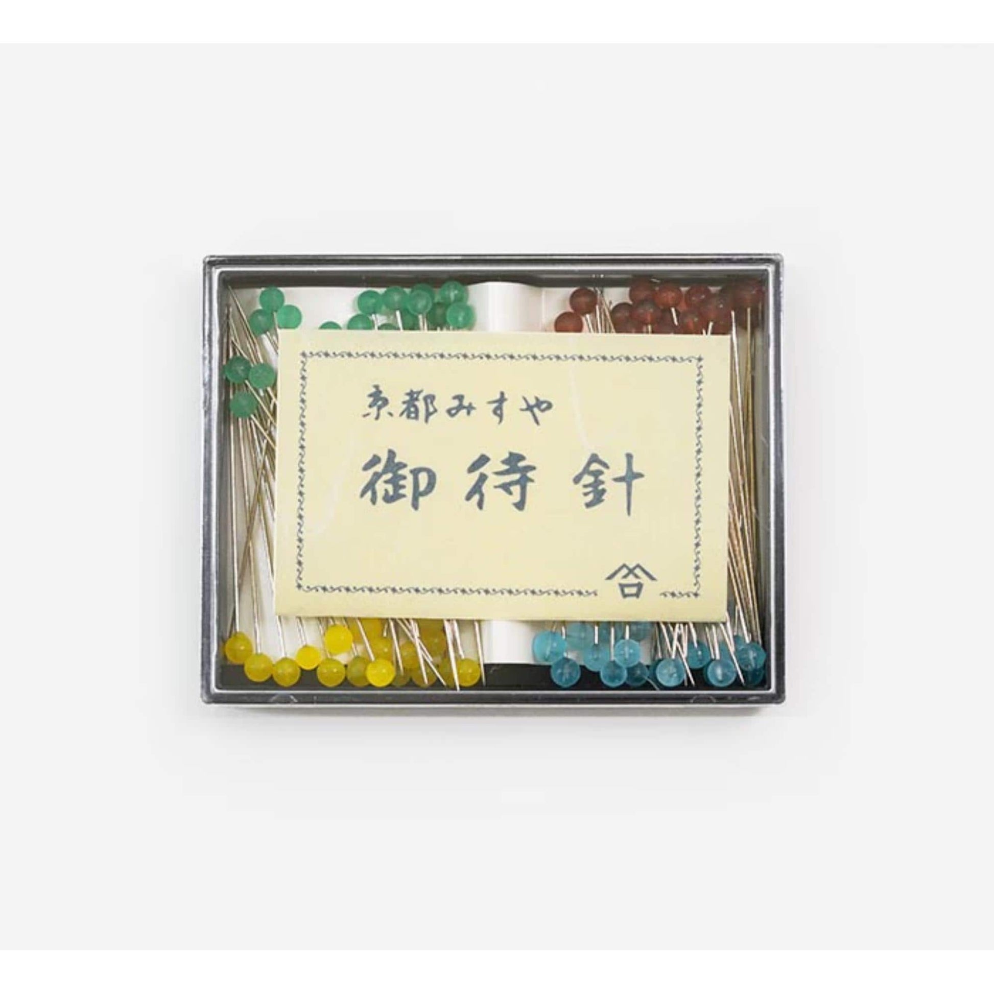 A small box containing a yellow sign with Japanese text and a variety of colorful push pins.
