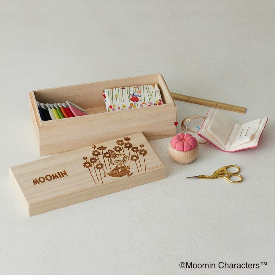 a wooden box with a floral design, a pair of gold scissors, and a small wooden ball with a pink exterior.
