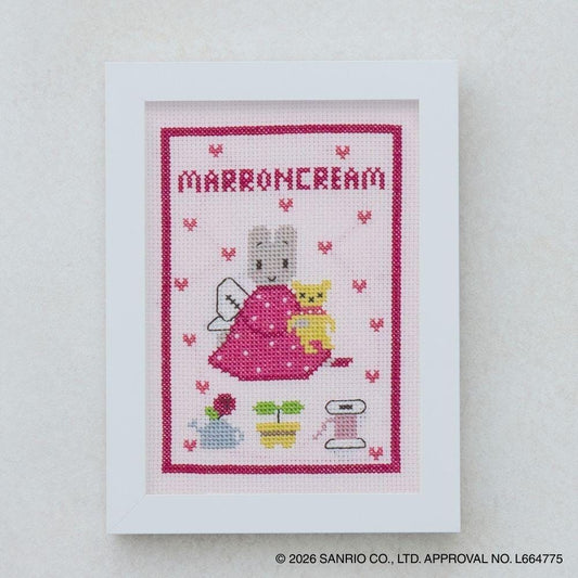 The image is a framed cross-stitch depicting a pink dress with a cat and a heart-shaped background, along with other small embroidered elements.