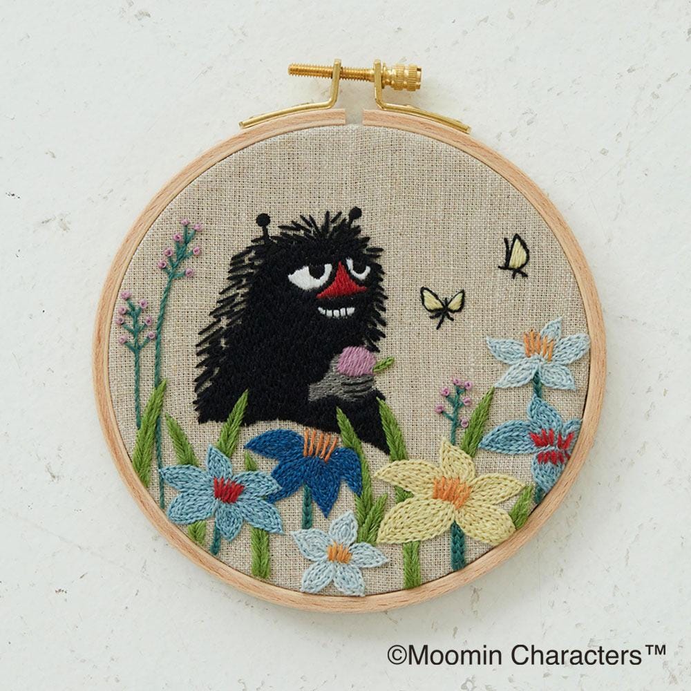 A hand-embroidered piece of art featuring a black creature surrounded by colorful flowers and butterflies.