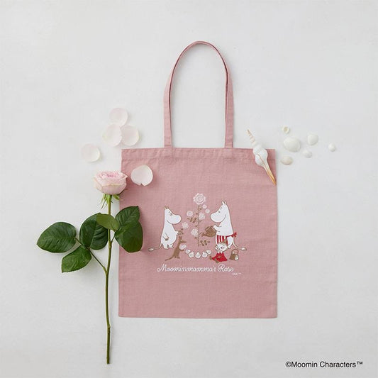 a pink tote bag with a printed design of two anthropomorphic animals, a rose, and the text "Moomin characters" on it, along with some seashells and a rose.