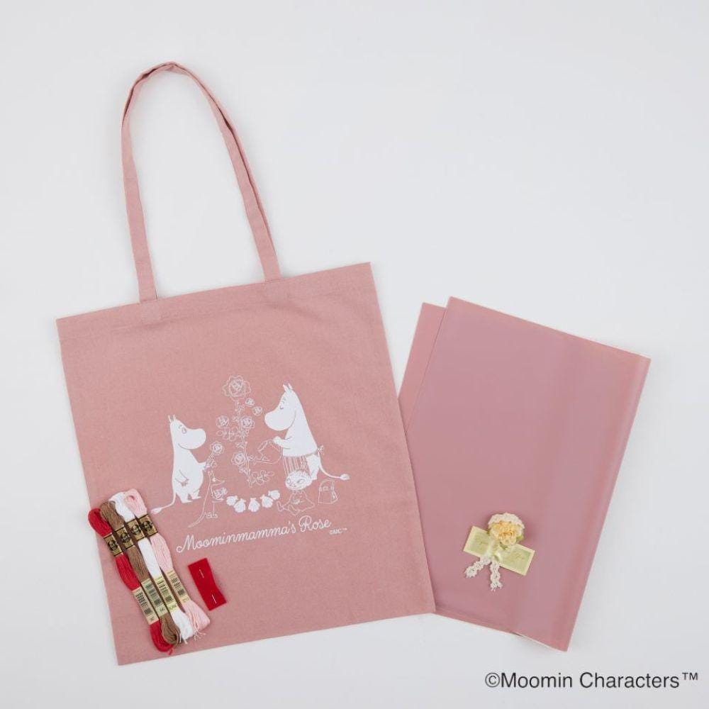 a pink tote bag with a white illustration of two Moomin characters, along with some accessories such as a pink ribbon, a small white flower, and a pink ribbon.