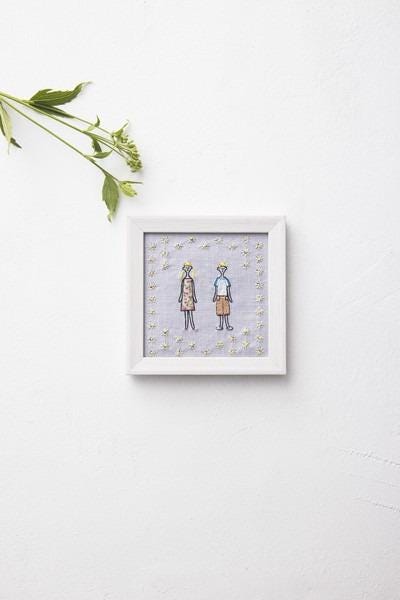 a framed artwork depicting two stylized human figures, with a background of small white flowers or stars.