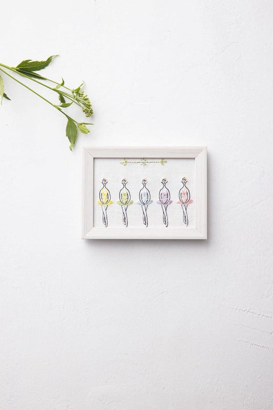 A framed artwork depicting five stylized human figures in various colors is displayed on a white wall, accompanied by a green plant.