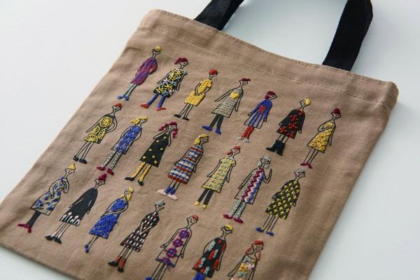 a beige tote bag with a unique embroidered design of various stylized human figures in different outfits.