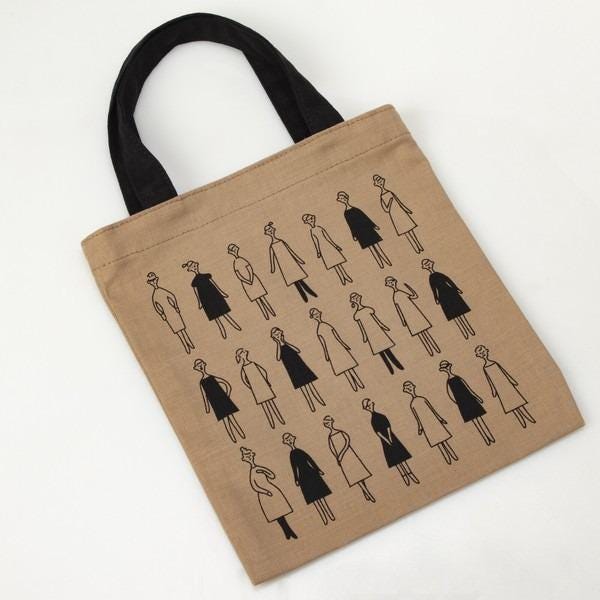 a beige tote bag with a repeating pattern of black silhouettes of women in various poses and outfits.