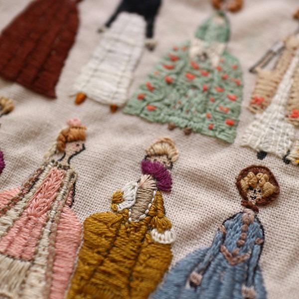 a close-up view of a hand-embroidered fabric with various colorful and detailed designs of women's dresses.