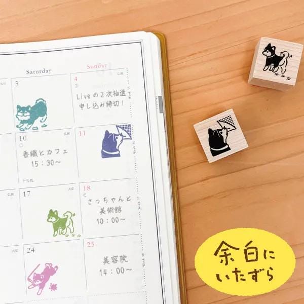 a calendar with a dog stamp on it, along with a wooden stamp and a yellow sticker with Japanese text on a wooden surface.