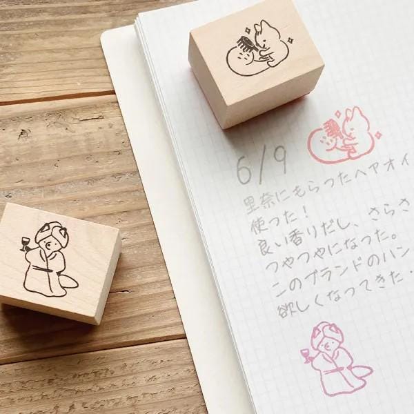 a wooden stamp with a cartoon character and a handwritten note on a notebook with Japanese text.