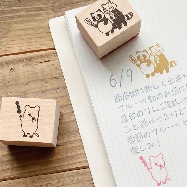 a wooden stamp with a cute cartoon character, a handwritten note on a notebook, and a small wooden stamp with a cute cartoon character.